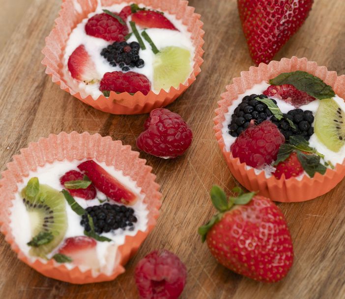 Eis-Joghurt in kleinen Muffin-Förmchen mit Obst auf einem Holzbrett