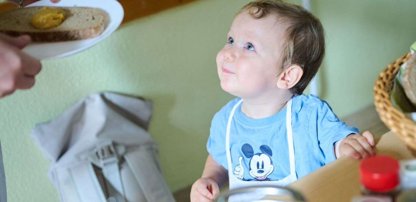 Ein kleines Kind guckt nach oben zu einem Teller mit einem Brot
