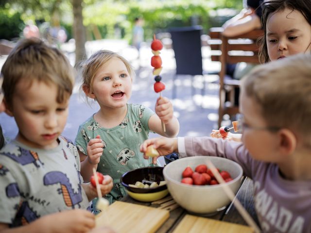 Ein Kind hält einen Holzspieß mit Obst und Beeren in die Höhe