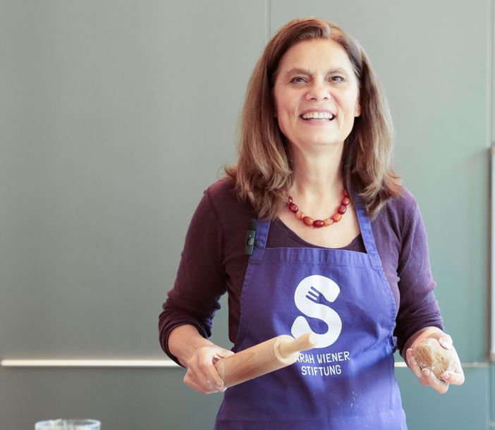 Sarah Wiener mit Nudelholz lacht in die Kamera