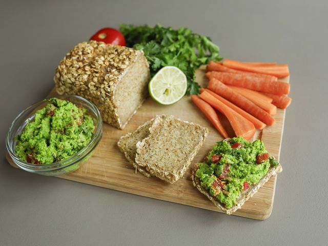 Auf einen Holzbrett sieht man die zubereitet Erbsenguacamole angerichtet mit Brot.