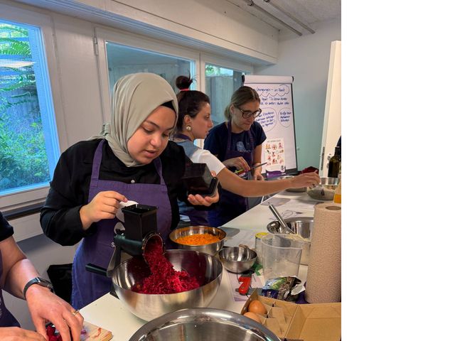 Mehrere Personen bereiten Essen zu, eine Frau häckselt Rote Bete.