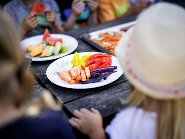 Rohkost liegt auf Tellern auf einem Tisch. Kinder sitzen um den Tisch herum.