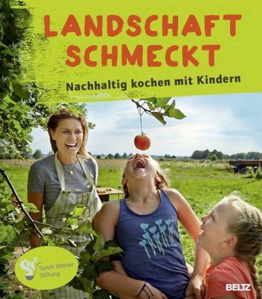 Buchcover von "Landschaft schmeckt". Stiftungsgründerin Sarah Wiener mit zwei Kindern auf einer Wiese mit einem Apfelbaum. 