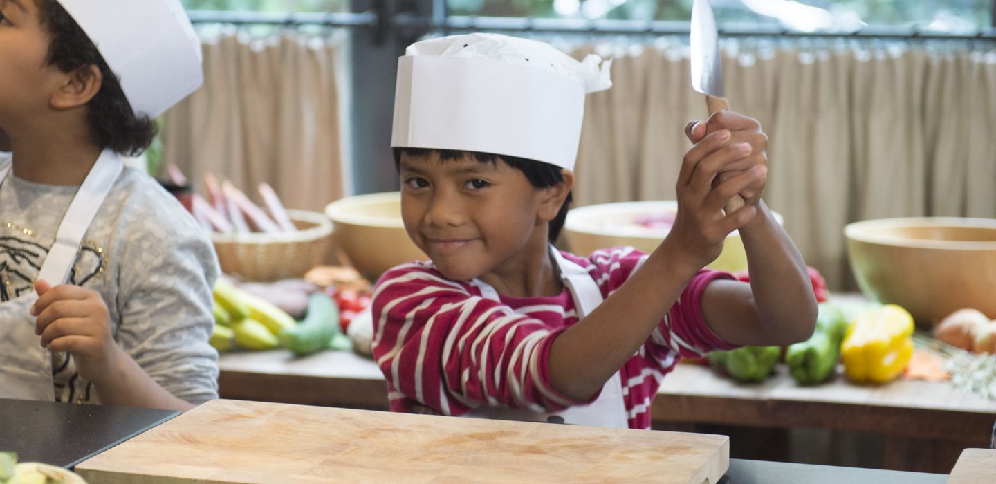 Ein Kind vor einem Holzbrett hält ein Messer in die Höhe