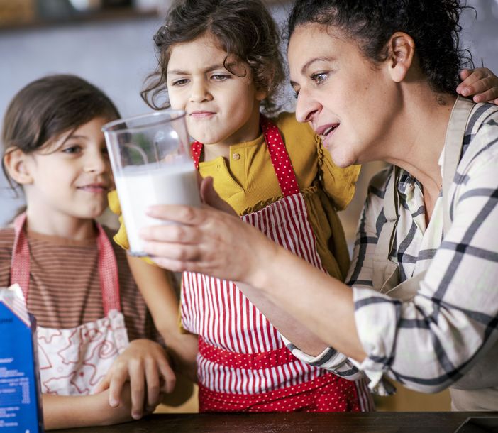 Eine Frau guckt mit zwei Kindern einen Becher Milch an