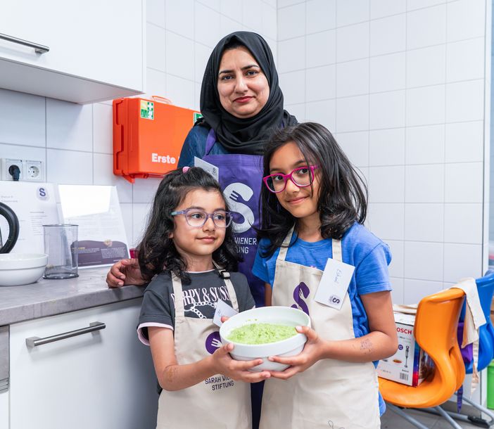 Eine Frau und zwei Kinder in einer Küche, die Kinder halten eine Salatschale