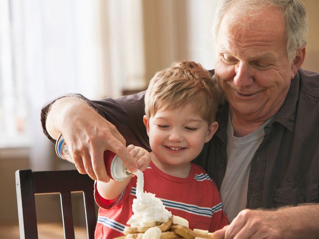 Ein älterer Mann mit Kind auf dem Schoß macht Sprühsahne auf Waffeln