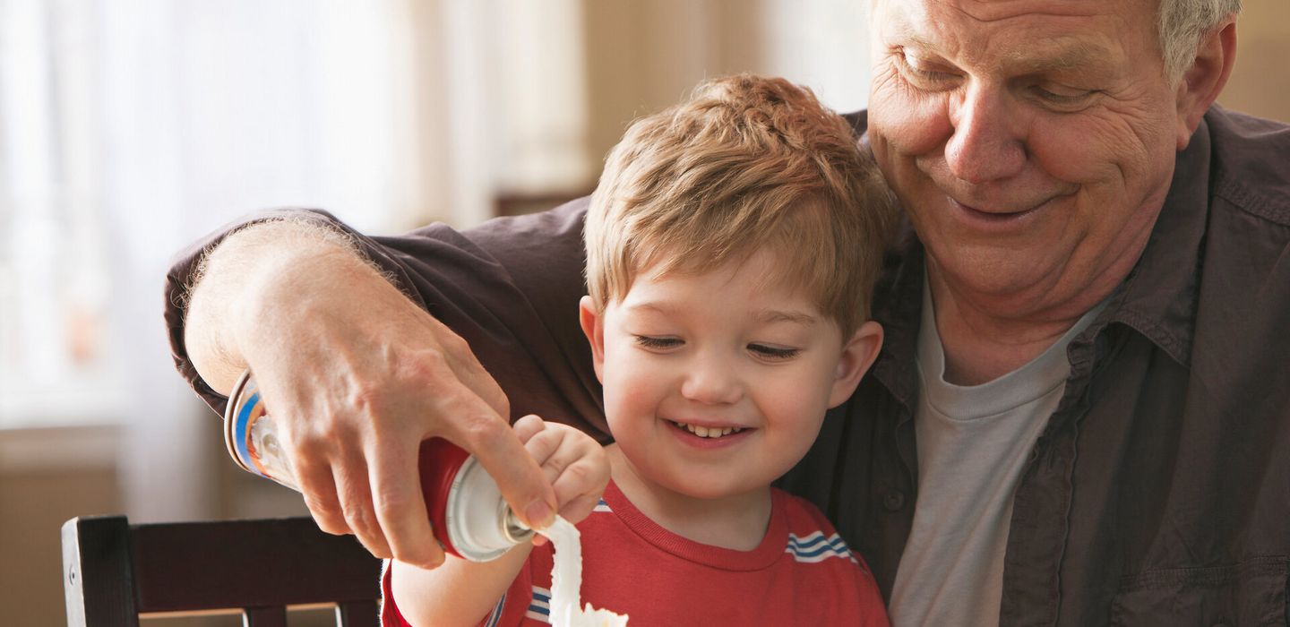 Ein älterer Mann mit Kind auf dem Schoß macht Sprühsahne auf Waffeln