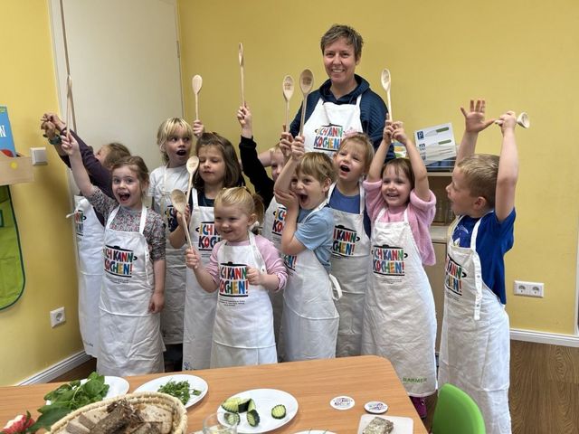 Kinder und eine Erwachsene jubeln mit Kochlöffeln in den Händen