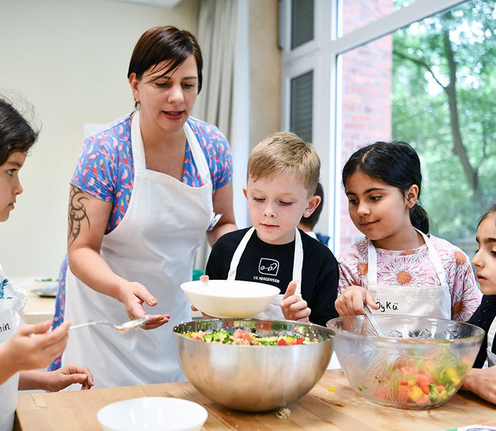 Lehrerin und drei Kinder stehen über eine Schüssel gebeugt