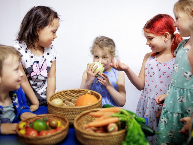 Eine Kindergruppe steht um einem Tisch voller Gemüse und erforscht die verschiedenen Sorten neugierig.