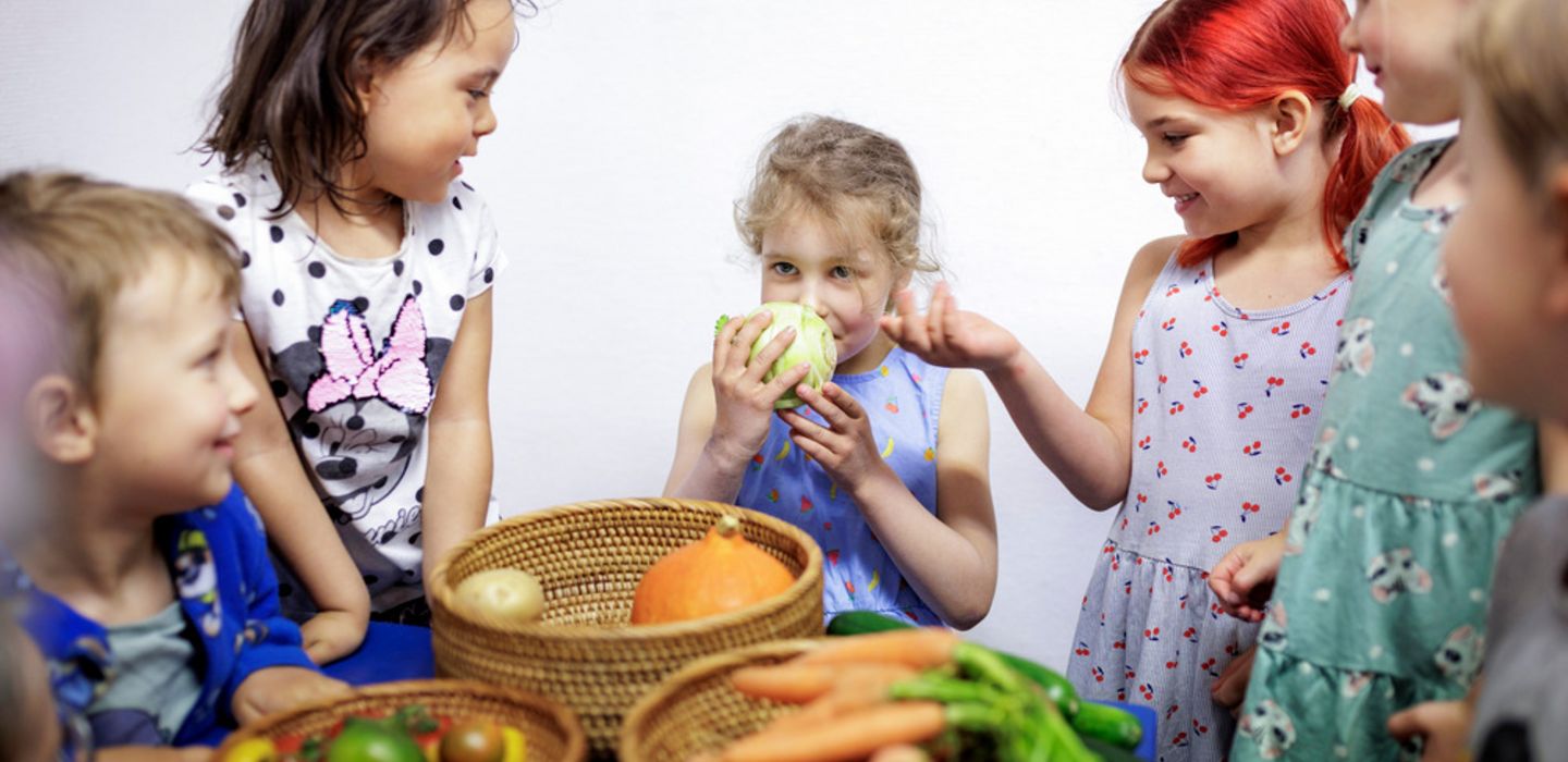 Eine Kindergruppe steht um einem Tisch voller Gemüse und erforscht die verschiedenen Sorten neugierig.