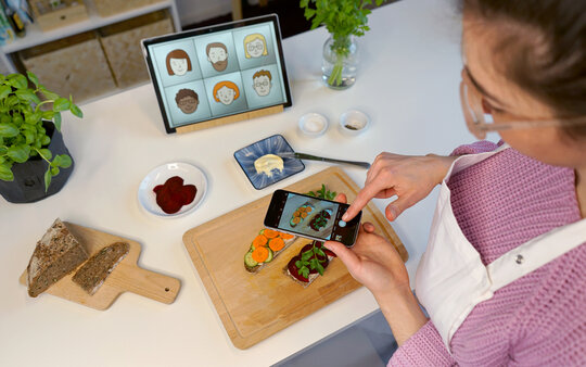 Eine Teilnehmerin an einer Ich kann kochen! Online-Fortbildung fotografiert mit einem Smartphone belegte Brote. Dies ist ein Praxisteil der Selbstlernphase der Online-Fortbildung.