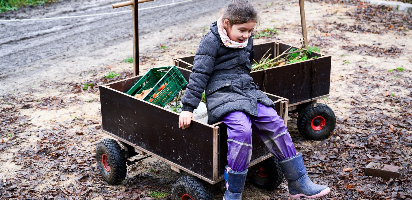 Ein Kind sitzt auf einem Bollerwagen mit Gemüse
