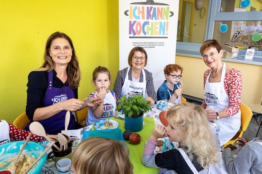 Sarah Wiener sitzt mit Köchinnen und Kindern um einen Esstisch