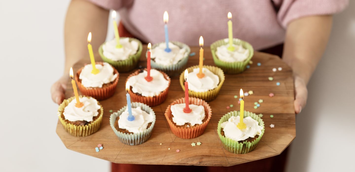 Muffins mit bunten Kerzen auf einem Holzbrett 