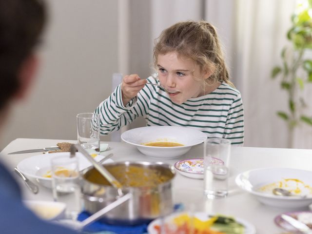 Mädchen sitzt am Küchentisch und isst Suppe