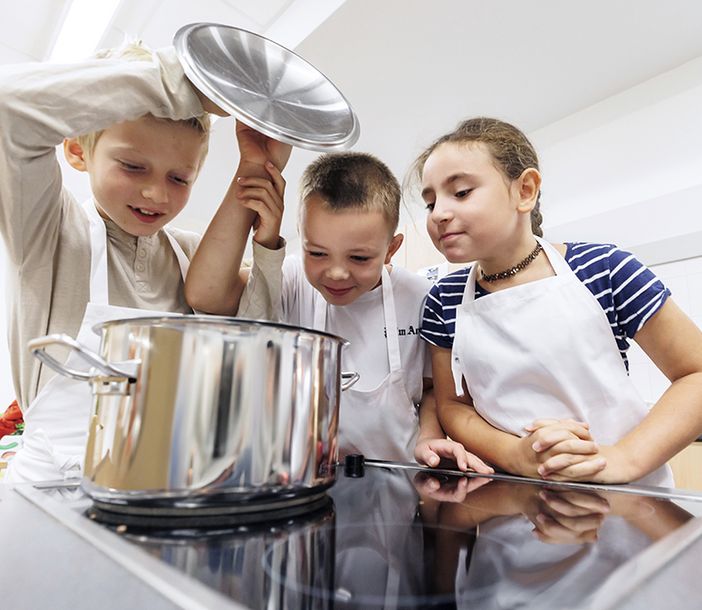 Drei Kinder schauen in einen Kochtopf