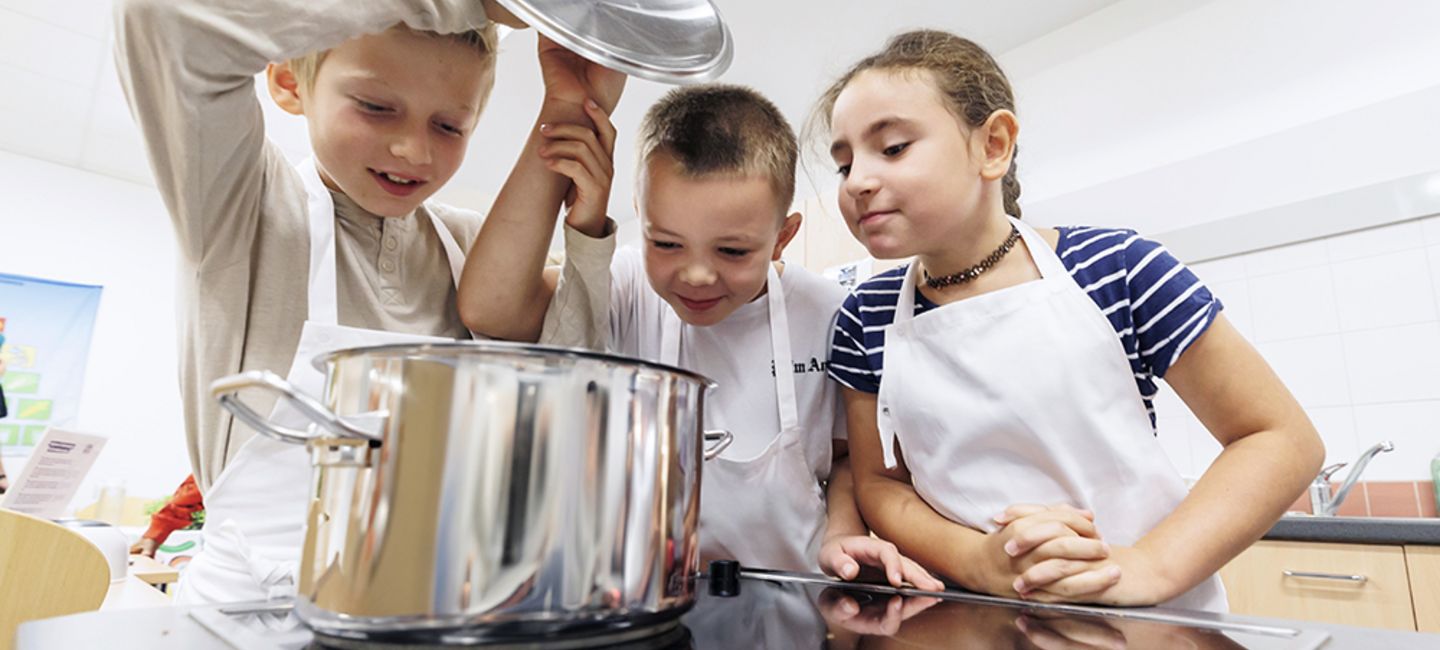 Drei Kinder schauen in einen Kochtopf