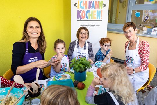 Sarah Wiener sitzt gemeinsam mit Kindern und Köchinnen am Esstisch