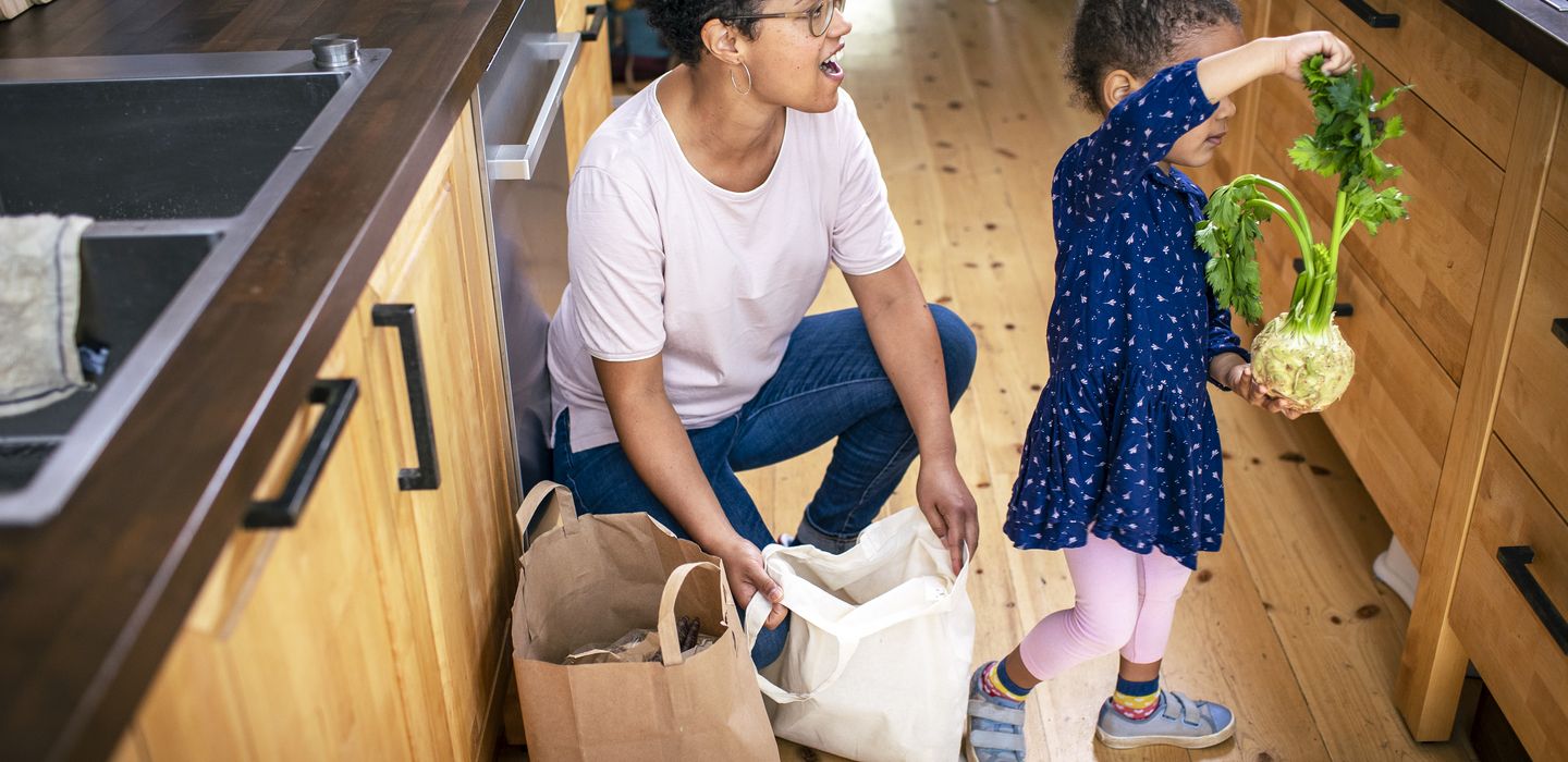 Eine Erwachsene kniet neben Einkauftüten, ein Kind holt Knollensellerie heraus