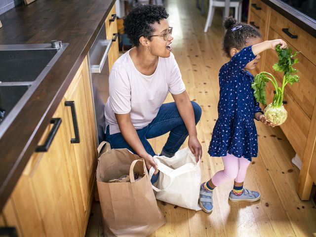 Eine Erwachsene kniet neben Einkauftüten, ein Kind holt Knollensellerie heraus